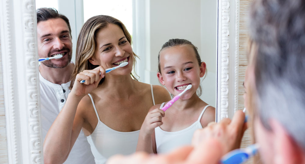 Parents and daughter brushing their teeth in the bathroom.