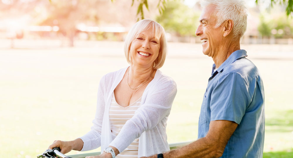 Senior couple riding bikes in a park | Restoration Dentistry